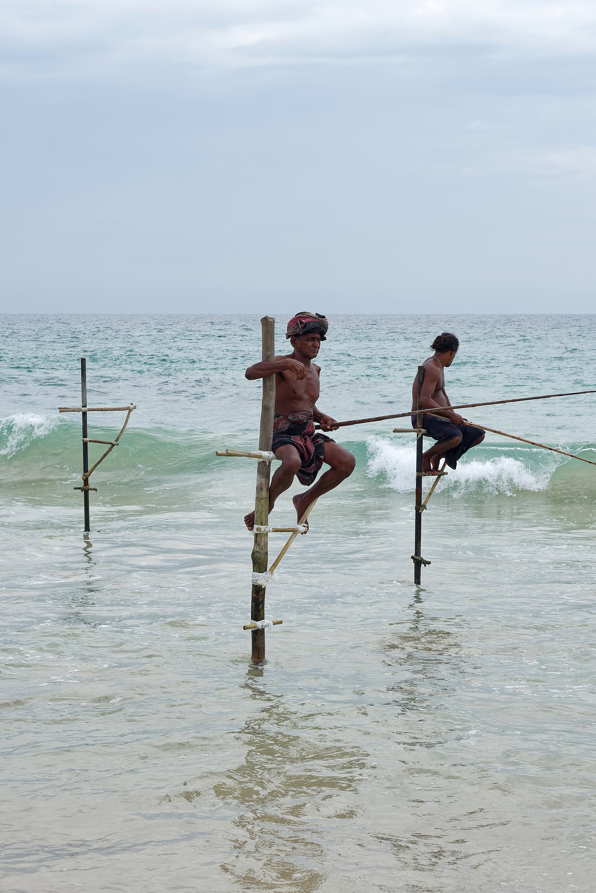 Traditional stilt fishermen perched on poles in shallow water near Galle